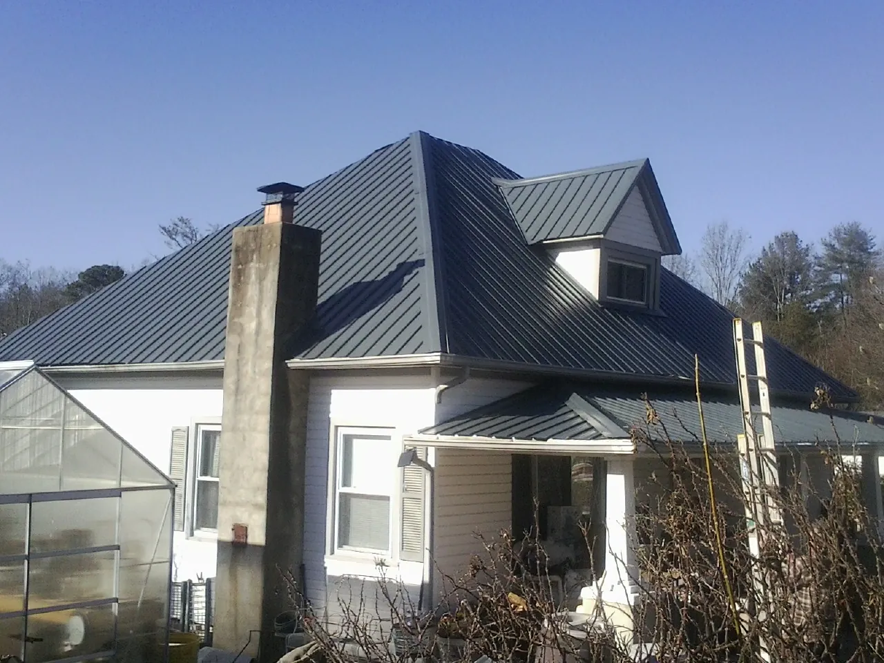 Dark blue standing seam metal roof on a white farmhouse with dormer — Slate & Tile Roof Repair by Roofing Brothers in Port Sanilac