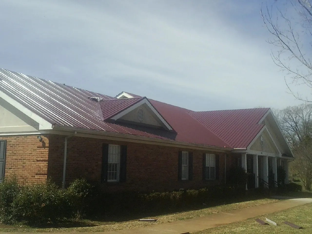 Red metal roof with gabled entries on a long brick building, from a Hail Damage Roof Repair job in Port Sanilac
