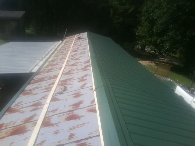 Old rusted panels beside newly installed green metal roofing — Wind Damage Roof Repair by Roofing Brothers in Port Sanilac