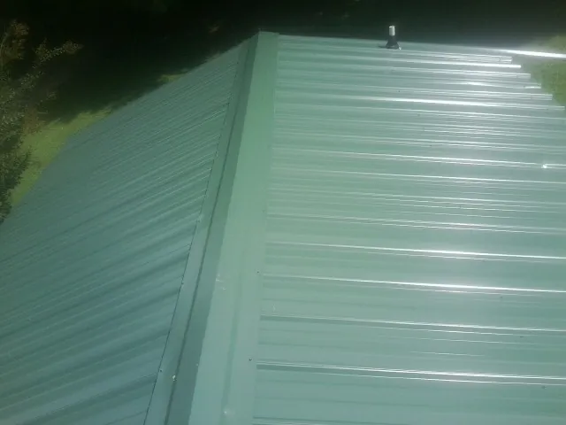 New green metal panels meeting at the ridge of a roof — Flat Roof Repair work by our crew in Port Sanilac