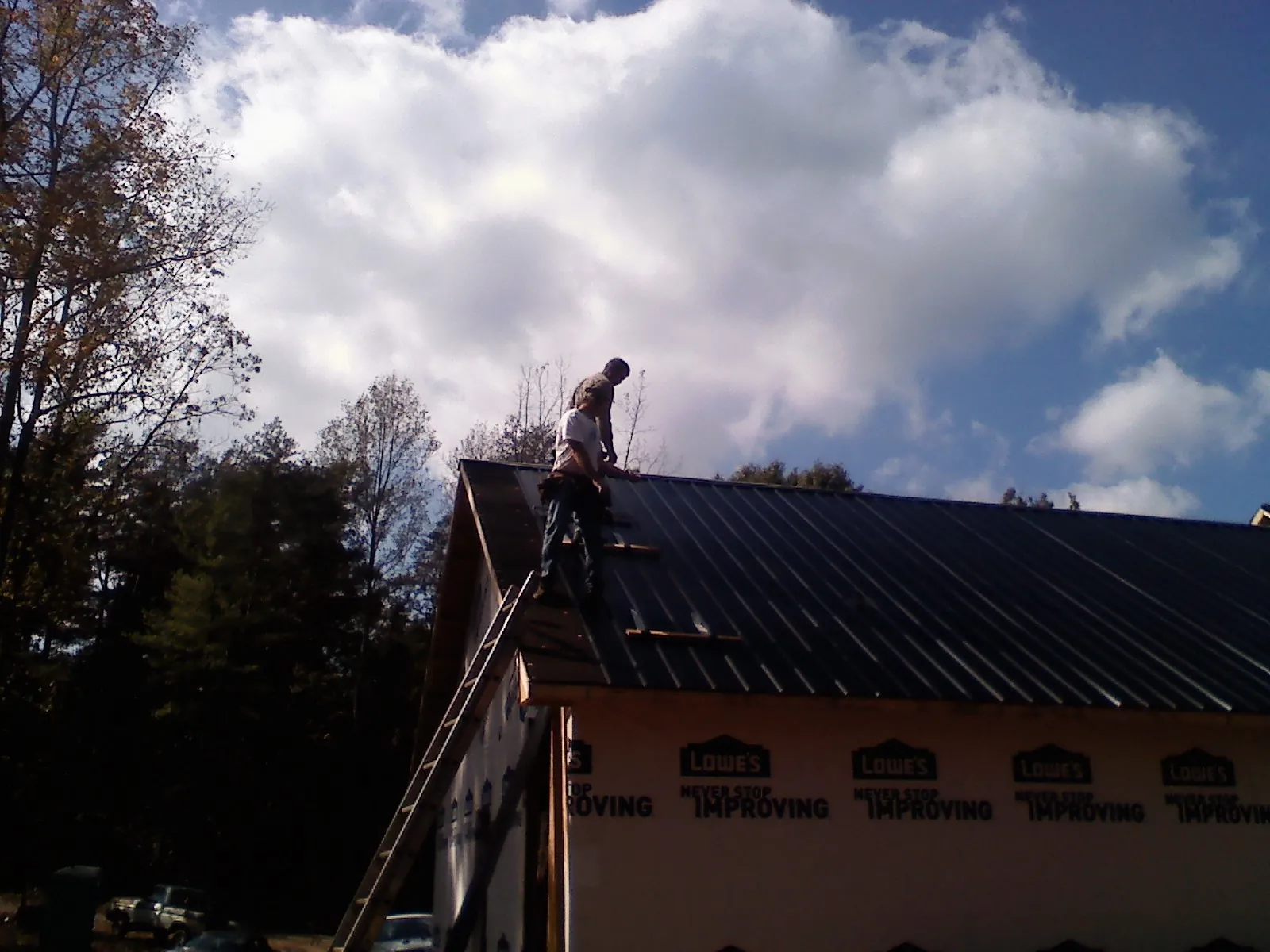 Roofer fastening dark metal panels high against a cloudy sky, from a Roof Inspection job in Port Sanilac