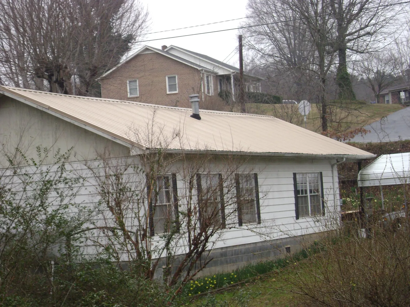 Tan metal roof on a white sided house set into a hillside — Commercial Roofing by Roofing Brothers in Port Sanilac