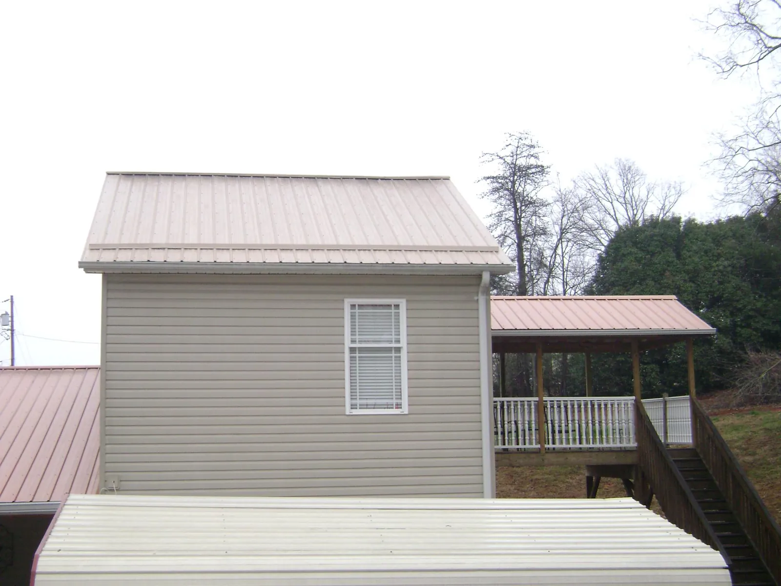Tan metal roofs on a two story addition and attached porch, from a Roof Replacement job in Port Sanilac